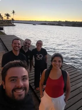 Minoru Raphael em selfie com três pessoas à beira de um lago ao pôr do sol, em Brasília