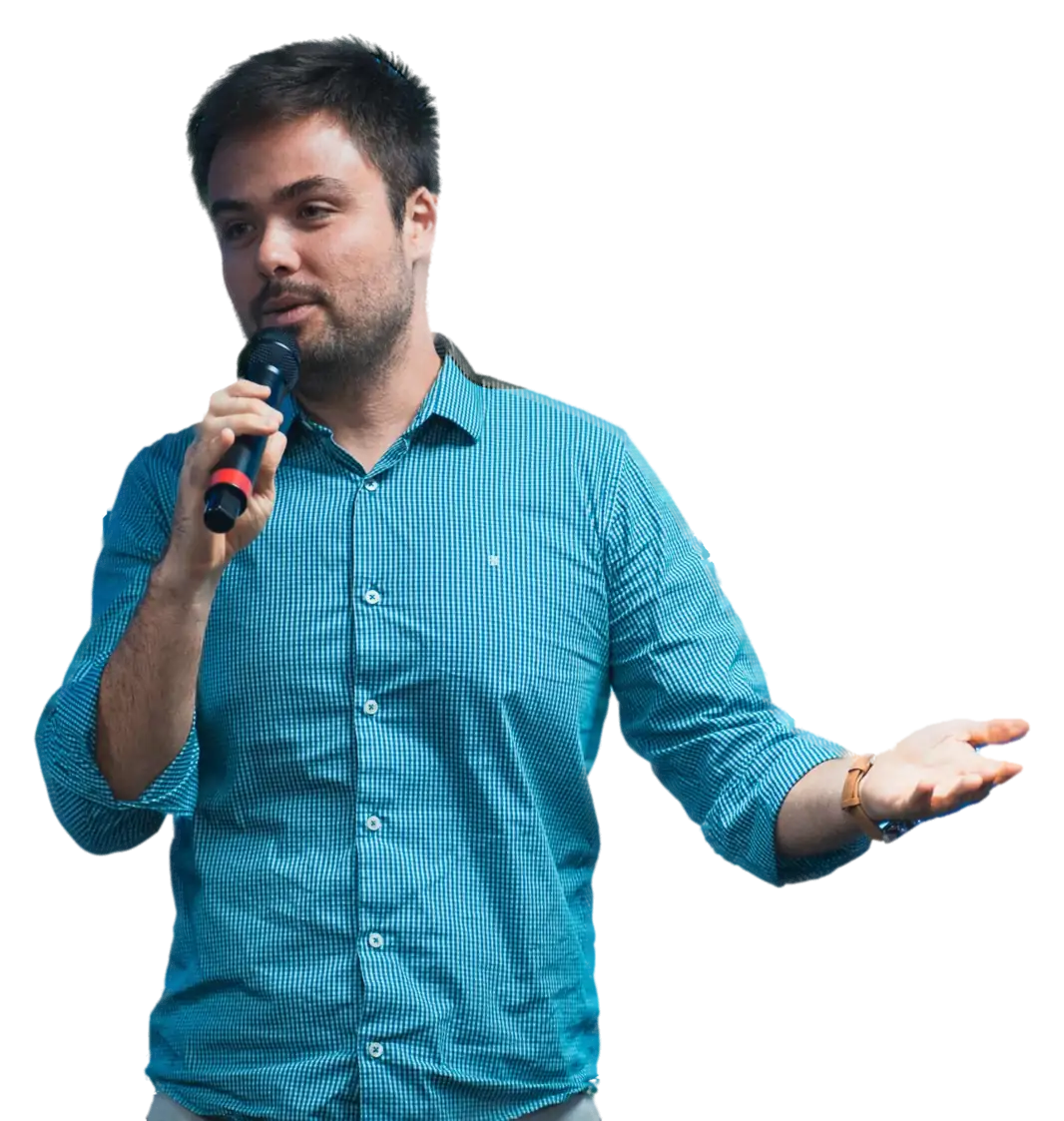 Minoru Raphael de camisa azul xadrez, falando ao microfone com o braço aberto