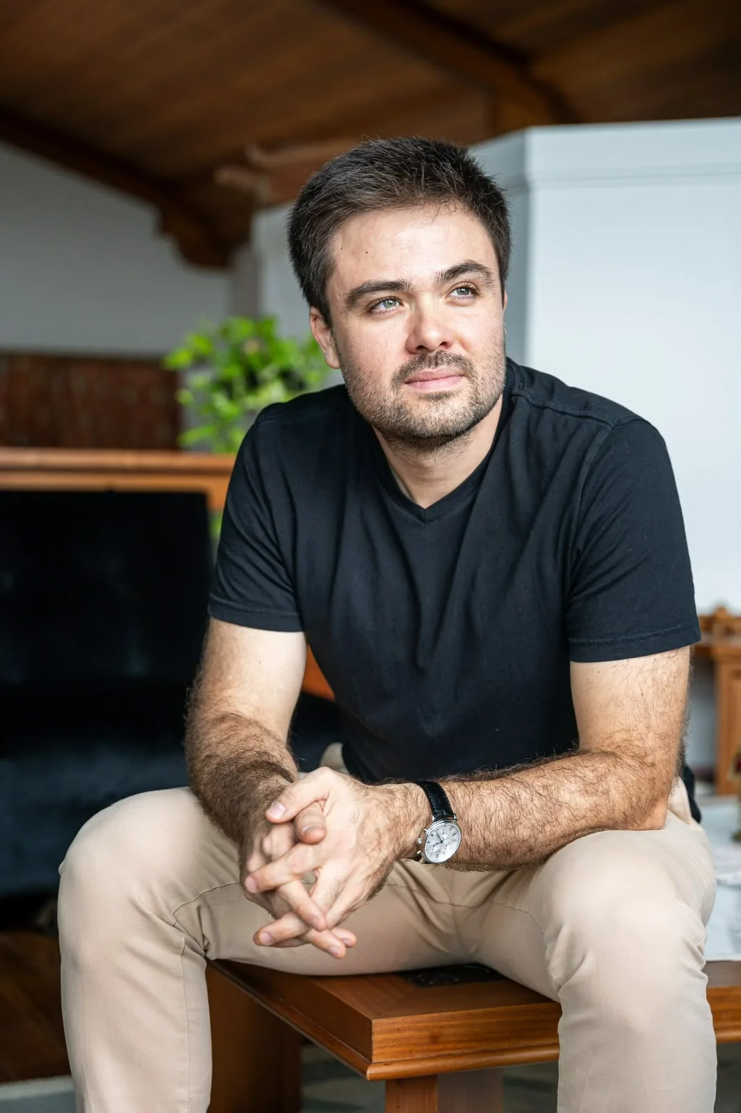 Minoru Raphael sentado, de camiseta preta e mãos entrelaçadas, olhando para o lado num ambiente com teto de madeira